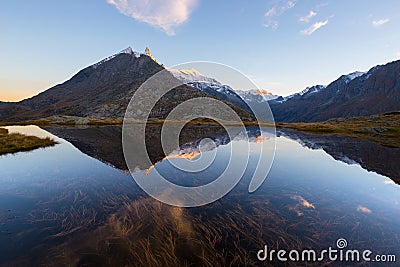 Camping with tent near high altitude lake on the Alps. Reflection of snowcapped mountain range and scenic colorful sky at sunset. Stock Photo