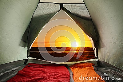 Camping tent with sleeping bags near river at sunset Stock Photo