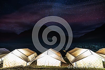 Camping under colourful sky full of stars. Glowing tents with silhouette mountains and sky full of star at Rangdum Monastery in In Stock Photo