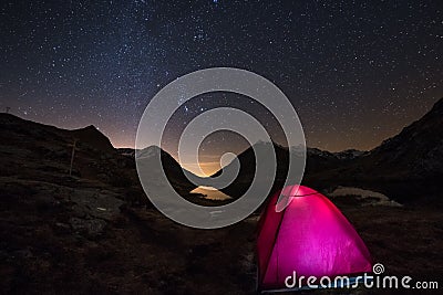 Camping under starry sky and Milky Way arc at high altitude on the italian french Alps. Glowing tent in the foreground. Adventure Stock Photo