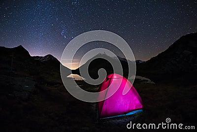 Camping under starry sky and Milky Way arc at high altitude on the italian french Alps. Glowing tent in the foreground. Adventure Stock Photo