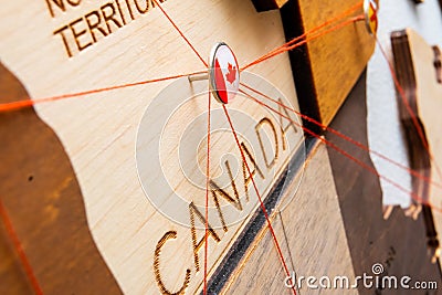 Canada flag on the pushpin and red threads on the wooden map Stock Photo