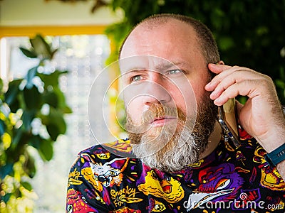 Candid photo of adult worried bearded man talking by smartphone Stock Photo