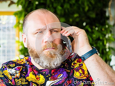 Candid photo of adult worried bearded man talking by smartphone Stock Photo