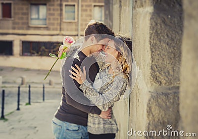 Candid portrait of beautiful European couple with rose in love kissing on street alley celebrating Valentines day Stock Photo