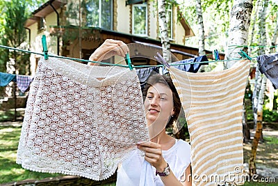 Candid real life portrait of young adult beautiful attractive caucasian woman hanging up fresh washed family clothes on birch tree Stock Photo