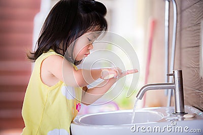 Candid short one little Asian girl washing her hands. She casually scrubbed the soap on her two hands intently and joyfully. Stock Photo