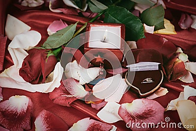 Candle and a diamond ring on a background of rose petals Stock Photo