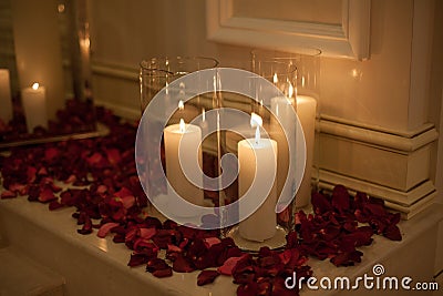 Candle surrounded by red rose petals with dreamy reflection Stock Photo