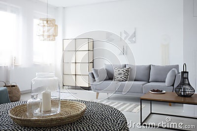 Candle on table in spacious white living room interior with patterned cushion on grey couch. Real photo Stock Photo