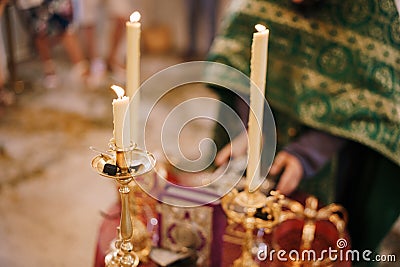 Candles are burning on candlesticks in front of the priest in the church Stock Photo