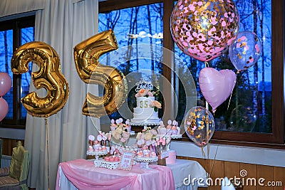 Candy bar large table with tasty sweets near window. Celebrating thirty-five years with two tier white cake with pink roses. Happy Stock Photo