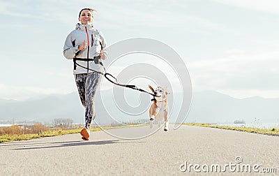 Canicross exercises. Female runs with his beagle dog and happy smiling. Autumn spring outdoor sport activity Stock Photo