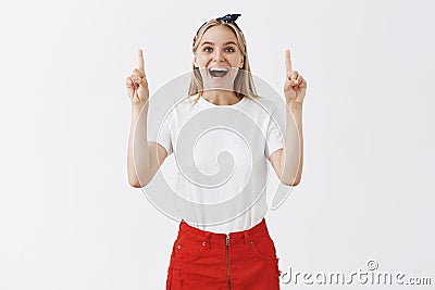 Cannot stop enjoing life. Portrait of charming carefree blonde female in stylish clothes, raising index fingers to point Stock Photo