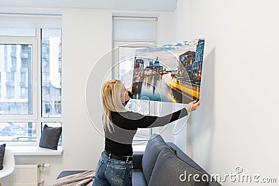 Canvas print with gallery wrap. Woman hangs photography on white wall. Hands holding photo canvas print. Stock Photo