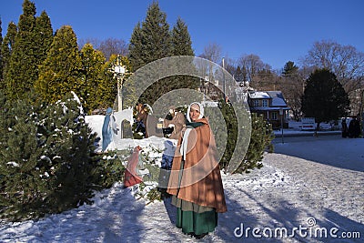 Pretty smiling woman dressed up in 17th century costume in front of a wooden Nativity display Editorial Stock Photo