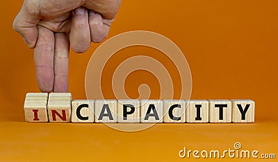 Capacity or incapacity symbol. Businessman turns wooden cubes and changes the word `incapacity` to `capacity`. Beautiful orang Stock Photo