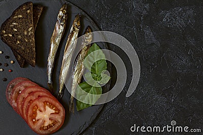 Capelin cold smoked fish on a round slate plate on a black-gray Stock Photo