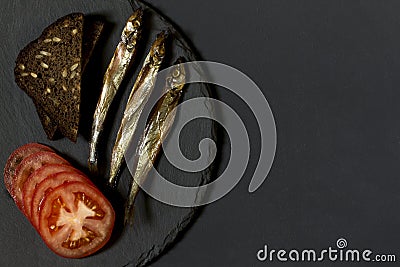 Capelin fish of cold smoked on round slate plate on black background. Stock Photo