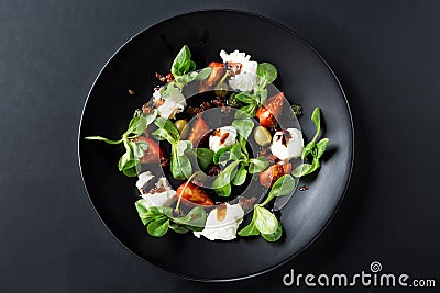 Caprese salad with mozzarella, tomato, basil and balsamic vinegar arranged on black plate and dark background. Top view Stock Photo