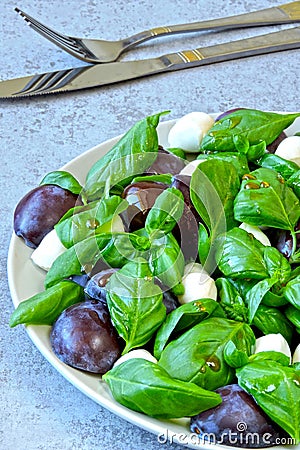 Caprese salad with plums. Fruity caprese. Healthy salad with basil and plums on a plate. Stock Photo