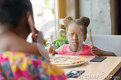 Capricious little girl with fancy hairstyle can`t wait for eating pizza. Stock Photo