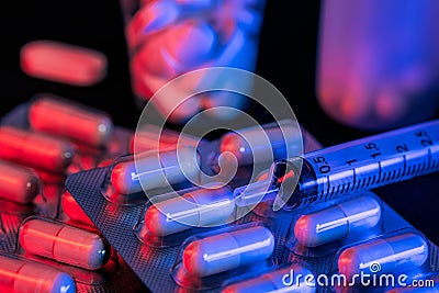 Capsule and pills medicines with syringe with black background and red and blue lights Stock Photo