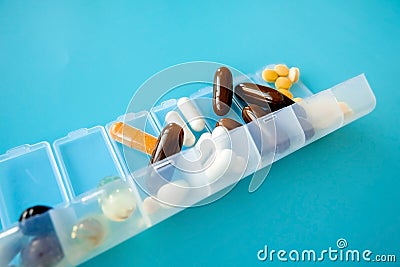 Capsules lie in a pill box on a blue background. Box for packing tablets for a week / Stock Photo