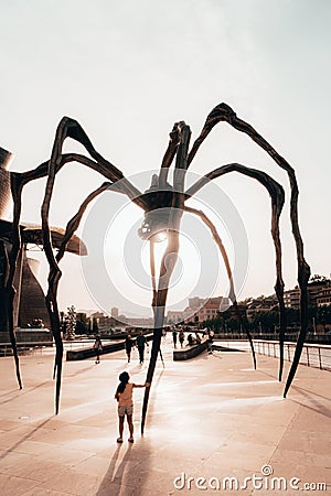 A captivating spider sculpture in Bilbao, its metal legs reaching out as a little girl finds wonder and fascination in its Editorial Stock Photo