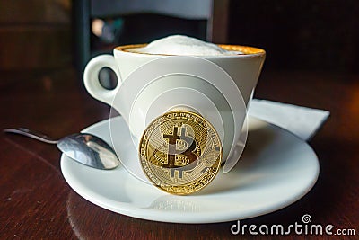 Capuccino and bitcoin gold coin on the table in cafe Stock Photo