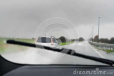 A car appearing clearly as a windscreen is wiped of rain by a wiper. Spray from cars can be seen on the wet road. Stock Photo