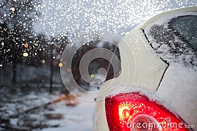 Car covered under white first snow. Red taillight, reverse lights and ice