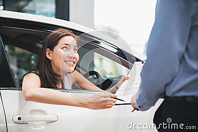 Car Dealership. The Asian woman checking a checklist with a smile for the salesman before hand over. Auto Leasing Business. Stock Photo