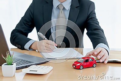 A car on desk envelope with man signing purchase documents in background. while hand complete the insurance policy, rental Stock Photo