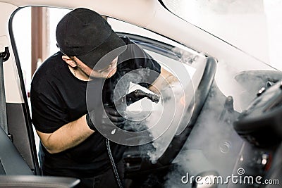 Car detailing, steam cleaning concept. Handsome man in black t-shirt and cap, worker of car wash center, cleaning car Stock Photo