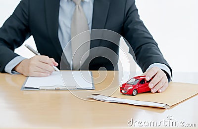 A Car on document envelope with man signing purchase documents in background. while hand complete the insurance policy, rental Stock Photo