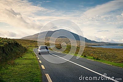 Car driving on empty scenic road trough nature by the lough inagh with mountains in the background Editorial Stock Photo