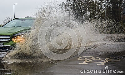 Car driving through Flooded road splashing sidewalk / pavements Editorial Stock Photo