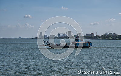 A car ferry crosses the Mekong River between Koh Dach / Silk Island and Phnom Penh, which appears in the background Editorial Stock Photo