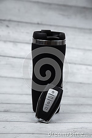 The car key is black with metal automatic buttons, leaning on a black thermocup for drinking on the road against a Stock Photo
