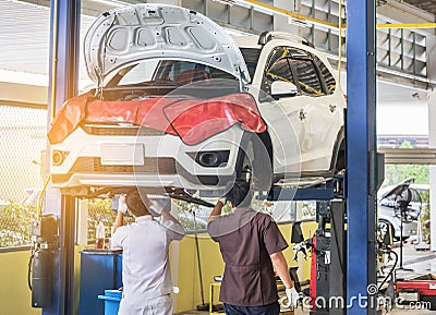 Car on lift to repair suspension in the garage with mechanics working underneath lifted car to change wheel hub Stock Photo