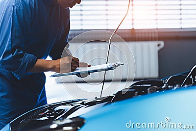 Car mechanic holding clipboard and checking to maintenance vehicle by customer claim order in auto repair shop garage. Engine Stock Photo