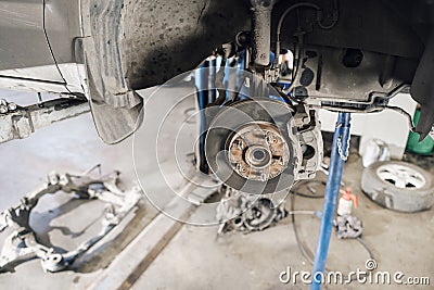 Car mechanic inspecting car wheel and repair suspension detail. Lifted automobile at repair service station. replacement Stock Photo