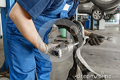 Car mechanic inspecting car wheel and repair suspension detail. Lifted automobile at repair service station. replacement Stock Photo