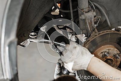 Car mechanic inspecting car wheel and repair suspension detail. Lifted automobile at repair service station. replacement Stock Photo