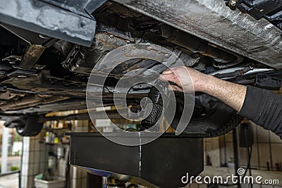 The car mechanic unscrews the diesel oil filter located in the oil pan, you can see the old oil flowing down in black. Stock Photo