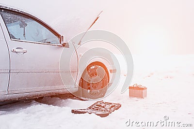A car with a raised hood on a background of a snowy field, tools and a discharged car battery near the car, the concept of a car Stock Photo
