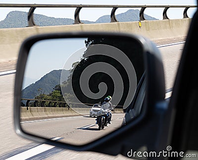 Car rear view mirror with the image of a biker approaching to overtake Stock Photo