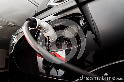 A car recharges its electric batteries inside a private garage with its own charging station, detail of the connected plug Stock Photo