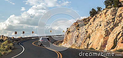 Car riding on a curvy road hairpin turn on a high terrace around a mountain with a scenic blue sky panorama Stock Photo